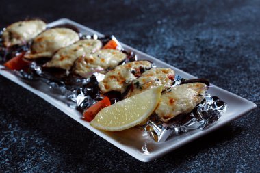 Erimiş peynirli haşlanmış istiridye. Büyük beyaz bir tabakta güzel istiridye servisi. Koyu mavi arka planda bir restoran için hazırlanmış deniz ürünleri..