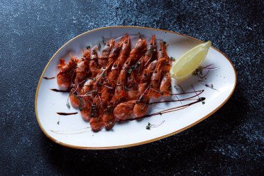 Üzerinde espaniol sosu olan küçük kırmızı karides. Güzel servis edilmiş haşlanmış karides. Koyu mavi arka planda bir restoran için hazırlanmış deniz ürünleri..