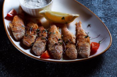 Kral balık büyük beyaz bir tabakta. Hamurda kızartılmış balık ve güzel bir sunum. Koyu mavi arka planda pişirilmiş deniz ürünleri..