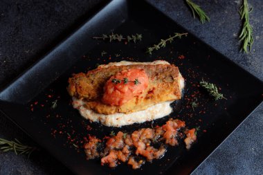 Izgara somon bifteği, taze domates, biber tohumu, biberiye, siyah tabakta kekik..