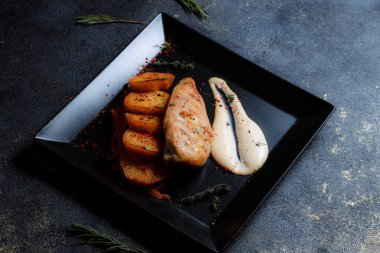 Baharatlı ızgara tavuk bifteği ve siyah bir tabakta fırında patates fotokopi alanı olan koyu dokulu bir arka planda..