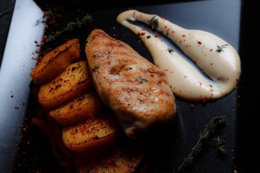 Baharatlı ızgara tavuk bifteği ve siyah bir tabakta fırında patates fotokopi alanı olan koyu dokulu bir arka planda..