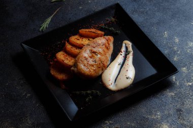 Baharatlı ızgara tavuk bifteği ve siyah bir tabakta fırında patates fotokopi alanı olan koyu dokulu bir arka planda..