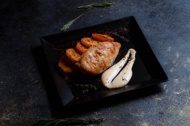 Baharatlı ızgara tavuk bifteği ve siyah bir tabakta fırında patates fotokopi alanı olan koyu dokulu bir arka planda..