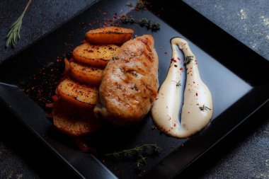 Baharatlı ızgara tavuk bifteği ve siyah bir tabakta fırında patates fotokopi alanı olan koyu dokulu bir arka planda..
