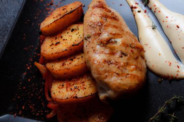 Baharatlı ızgara tavuk bifteği ve siyah bir tabakta fırında patates fotokopi alanı olan koyu dokulu bir arka planda..