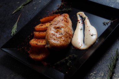 Baharatlı ızgara tavuk bifteği ve siyah bir tabakta fırında patates fotokopi alanı olan koyu dokulu bir arka planda..