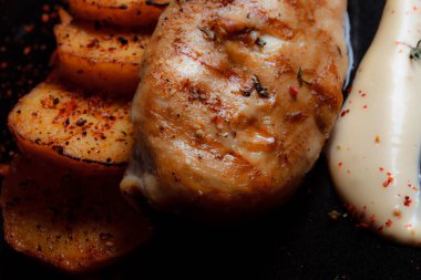 Baharatlı ızgara tavuk bifteği ve siyah bir tabakta fırında patates fotokopi alanı olan koyu dokulu bir arka planda..