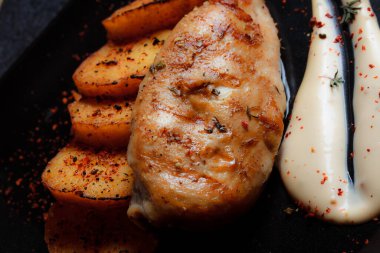 Baharatlı ızgara tavuk bifteği ve siyah bir tabakta fırında patates fotokopi alanı olan koyu dokulu bir arka planda..