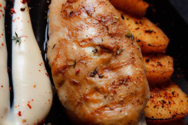 Baharatlı ızgara tavuk bifteği ve siyah bir tabakta fırında patates fotokopi alanı olan koyu dokulu bir arka planda..