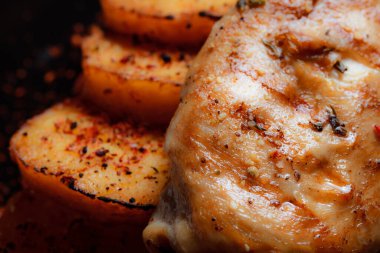 Baharatlı ızgara tavuk bifteği ve siyah bir tabakta fırında patates fotokopi alanı olan koyu dokulu bir arka planda..