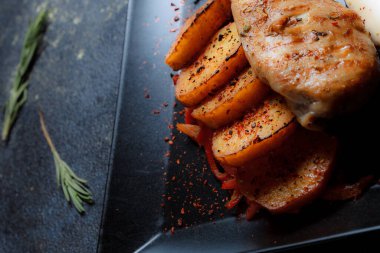 Baharatlı ızgara tavuk bifteği ve siyah bir tabakta fırında patates fotokopi alanı olan koyu dokulu bir arka planda..