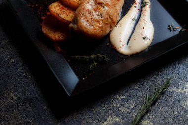 Baharatlı ızgara tavuk bifteği ve siyah bir tabakta fırında patates fotokopi alanı olan koyu dokulu bir arka planda..