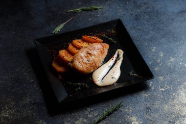 Baharatlı ızgara tavuk bifteği ve siyah bir tabakta fırında patates fotokopi alanı olan koyu dokulu bir arka planda..