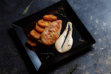 Baharatlı ızgara tavuk bifteği ve siyah bir tabakta fırında patates fotokopi alanı olan koyu dokulu bir arka planda..