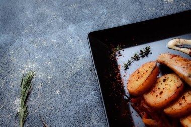 Baharatlı ızgara tavuk bifteği ve siyah bir tabakta fırında patates fotokopi alanı olan koyu dokulu bir arka planda..
