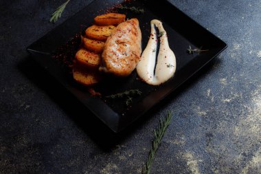 Baharatlı ızgara tavuk bifteği ve siyah bir tabakta fırında patates fotokopi alanı olan koyu dokulu bir arka planda..