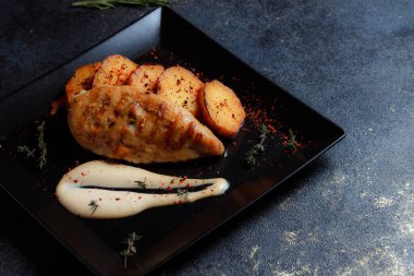 Baharatlı ızgara tavuk bifteği ve siyah bir tabakta fırında patates fotokopi alanı olan koyu dokulu bir arka planda..