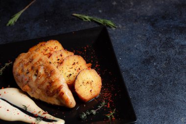 Baharatlı ızgara tavuk bifteği ve siyah bir tabakta fırında patates fotokopi alanı olan koyu dokulu bir arka planda..