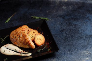 Baharatlı ızgara tavuk bifteği ve siyah bir tabakta fırında patates fotokopi alanı olan koyu dokulu bir arka planda..