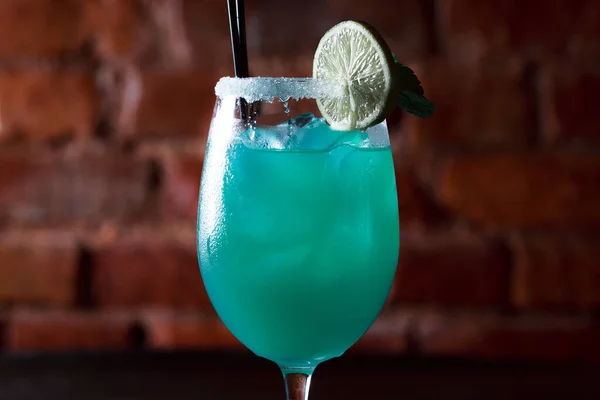Alcoholic cocktail blue lagoon. Green cocktail drink with lime on a dark blue textured background.