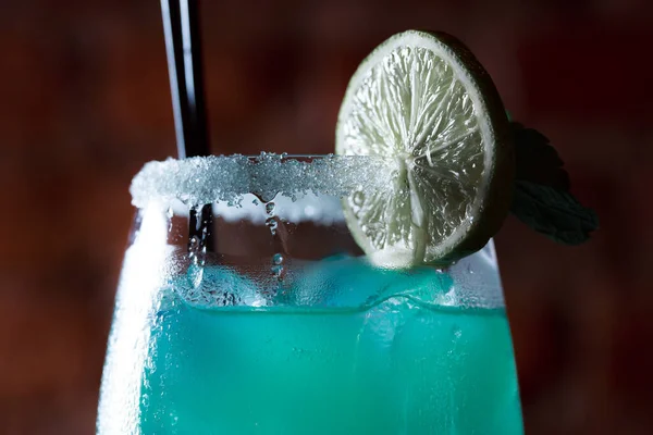 Alcoholic cocktail blue lagoon. Green cocktail drink with lime on a dark blue textured background.