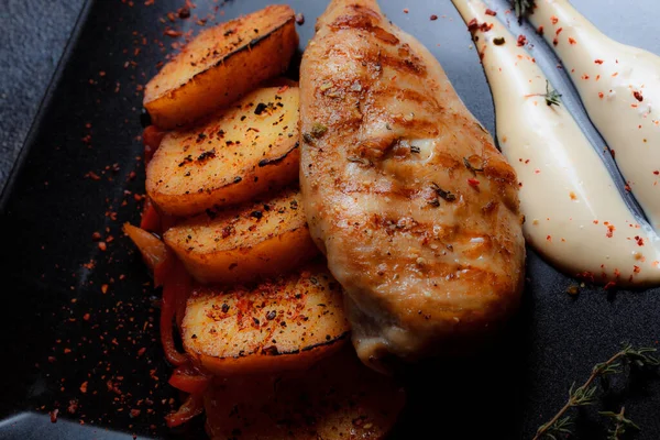 Baharatlı ızgara tavuk bifteği ve siyah bir tabakta fırında patates fotokopi alanı olan koyu dokulu bir arka planda..