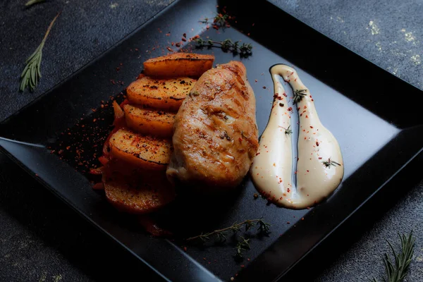 Baharatlı ızgara tavuk bifteği ve siyah bir tabakta fırında patates fotokopi alanı olan koyu dokulu bir arka planda..