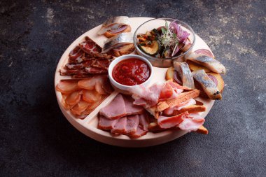 Ahşap çatal üzerinde atıştırmalıklar. Dilimlenmiş pastırma ve sosis. Bira için küçük aperatifler. Ekmek üstü balık şeklinde. Koyu dokuda yiyecek..