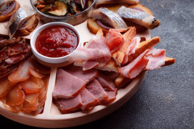 Ahşap çatal üzerinde atıştırmalıklar. Dilimlenmiş pastırma ve sosis. Bira için küçük aperatifler. Ekmek üstü balık şeklinde. Koyu dokuda yiyecek..