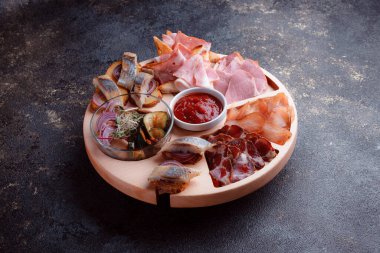 Ahşap çatal üzerinde atıştırmalıklar. Dilimlenmiş pastırma ve sosis. Bira için küçük aperatifler. Ekmek üstü balık şeklinde. Koyu dokuda yiyecek..