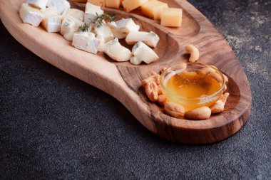 Tahta bir tahtanın üzerinde dilimlenmiş peynir. Bal ve fındıklı peynir servisi. Sağlıklı bir öğle yemeği konsepti olan sert peynir ve lacivert. Ziyafetler ve özel günler için tabaklar.