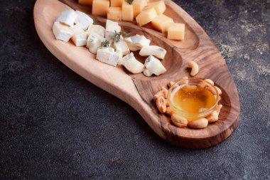 Tahta bir tahtanın üzerinde dilimlenmiş peynir. Bal ve fındıklı peynir servisi. Sağlıklı bir öğle yemeği konsepti olan sert peynir ve lacivert. Ziyafetler ve özel günler için tabaklar.
