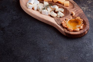 Tahta bir tahtanın üzerinde dilimlenmiş peynir. Bal ve fındıklı peynir servisi. Sağlıklı bir öğle yemeği konsepti olan sert peynir ve lacivert. Ziyafetler ve özel günler için tabaklar.