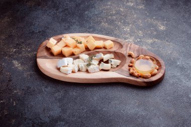 Tahta bir tahtanın üzerinde dilimlenmiş peynir. Bal ve fındıklı peynir servisi. Sağlıklı bir öğle yemeği konsepti olan sert peynir ve lacivert. Ziyafetler ve özel günler için tabaklar.