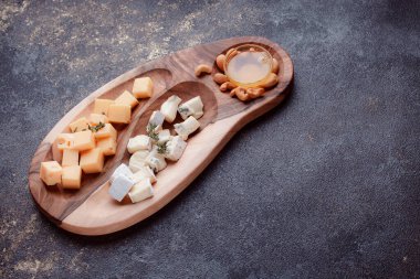 Tahta bir tahtanın üzerinde dilimlenmiş peynir. Bal ve fındıklı peynir servisi. Sağlıklı bir öğle yemeği konsepti olan sert peynir ve lacivert. Ziyafetler ve özel günler için tabaklar.