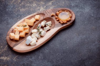 Tahta bir tahtanın üzerinde dilimlenmiş peynir. Bal ve fındıklı peynir servisi. Sağlıklı bir öğle yemeği konsepti olan sert peynir ve lacivert. Ziyafetler ve özel günler için tabaklar.