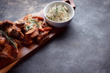 Bir set tabağı: kemiklerde büyük bir parça et, köy usulü ızgara patates, küçük bir lahana salatası, fasulye filizi, chia tohumu ve yeşil soğan. Orijinal servis ahşap kesme tahtasında..