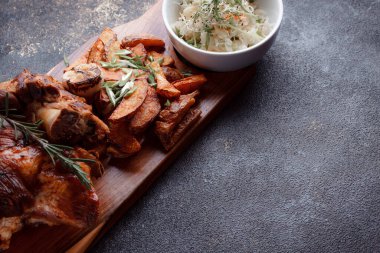 Bir set tabağı: kemiklerde büyük bir parça et, köy usulü ızgara patates, küçük bir lahana salatası, fasulye filizi, chia tohumu ve yeşil soğan. Orijinal servis ahşap kesme tahtasında..