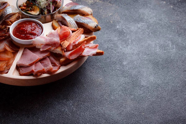 Ahşap çatal üzerinde atıştırmalıklar. Dilimlenmiş pastırma ve sosis. Bira için küçük aperatifler. Ekmek üstü balık şeklinde. Koyu dokuda yiyecek..