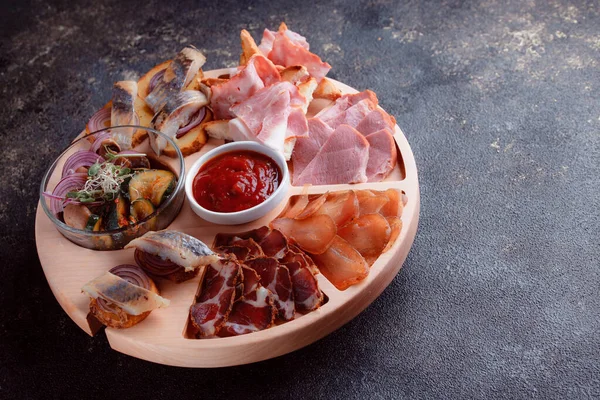 Ahşap çatal üzerinde atıştırmalıklar. Dilimlenmiş pastırma ve sosis. Bira için küçük aperatifler. Ekmek üstü balık şeklinde. Koyu dokuda yiyecek..