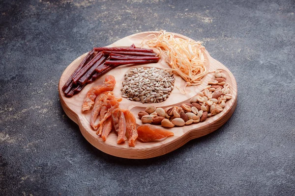 Snacks for beer on wooden utensils. Sliced dried fish in pieces and in the form of sticks. Mix of nuts and cheeses. Food on a dark texture background. Eco-friendly tableware.