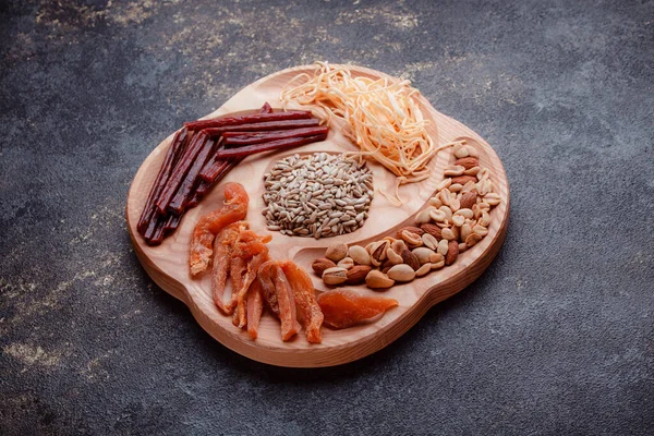 Snacks for beer on wooden utensils. Sliced dried fish in pieces and in the form of sticks. Mix of nuts and cheeses. Food on a dark texture background. Eco-friendly tableware.