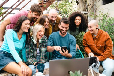 Genç öğrenciler bilgisayarın önünde akıllı telefondan içeriği izlerken çevrimiçi yayınlıyorlar. Çevrimiçi görselleştirmeyi cep telefonundan kontrol eden insanlar kavramı.