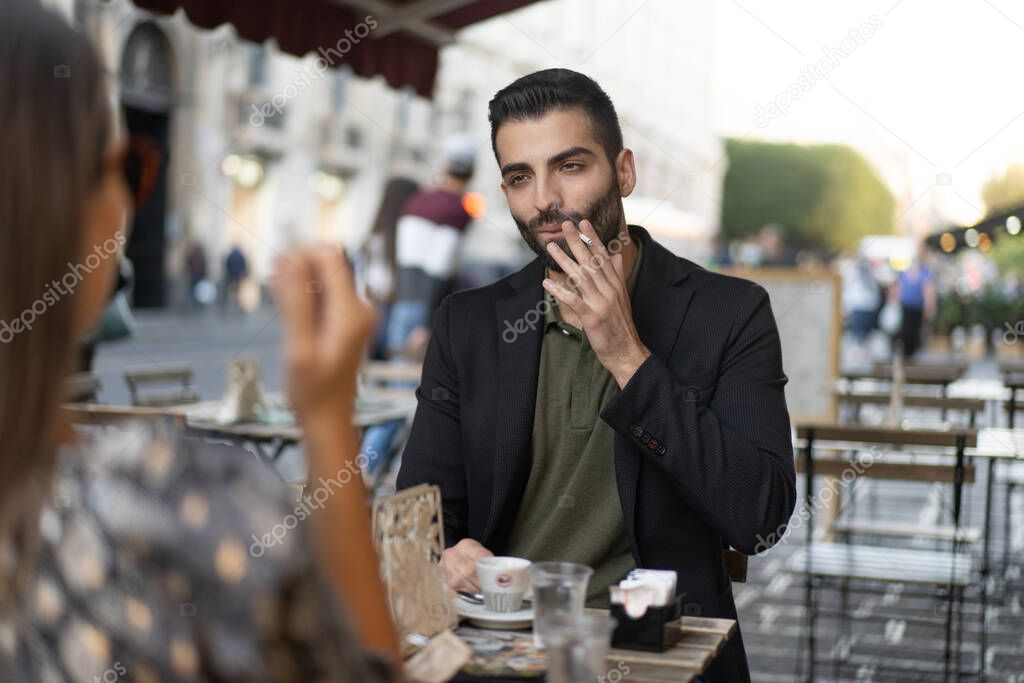 Young guy sitting on a table with a woman drinking espresso coffee and smoking cigarettes - dating or business concept.