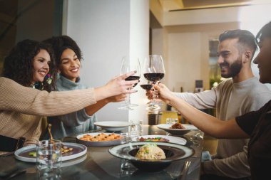 Şarap kadehlerini tokuşturup arkadaşlarıyla restoranda kırmızı şarap içen çok ırklı bir arkadaş grubu.