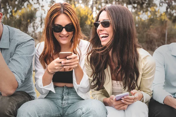 Bir grup modaya uygun genç dışarıda bir bankta oturup sohbet ediyorlar. Öğrenciler akıllı telefonları kullanarak birlikte eğleniyorlar..