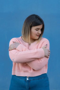Havalı, kıvrımlı bir kadın modeli. Kendini kucaklıyor, gözleri kapalı. Vücut pozitifliği kavramı ve kendine güveni yüksek insanlar.