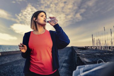 Tombul atlet kız koşusuna ara veriyor ve plastik şişeden su içiyor.