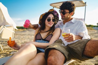 Yazın tatilde olan romantik bir çift sahilde şezlongda oturmuş meyve suyu ve beyaz şarap içiyor. Sağlıklı lüks yaşam tarzı konsepti